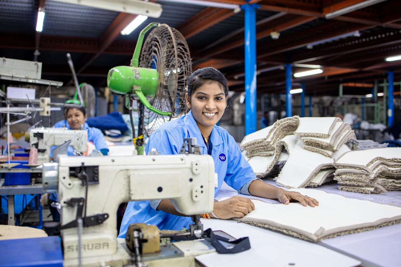 A smiling textile worker operating a sewing machine in a factory.